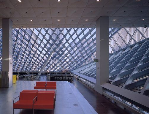 Modern interior with angular glass and expanded aluminium mesh architecture and two red chairs.