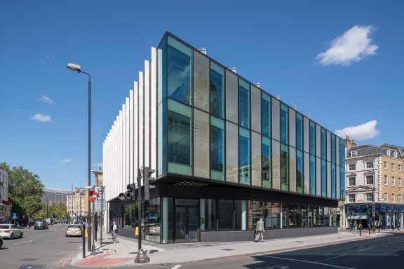 Modern building with large glass windows with metal mesh and a minimalist design, set against a clear blue sky.
