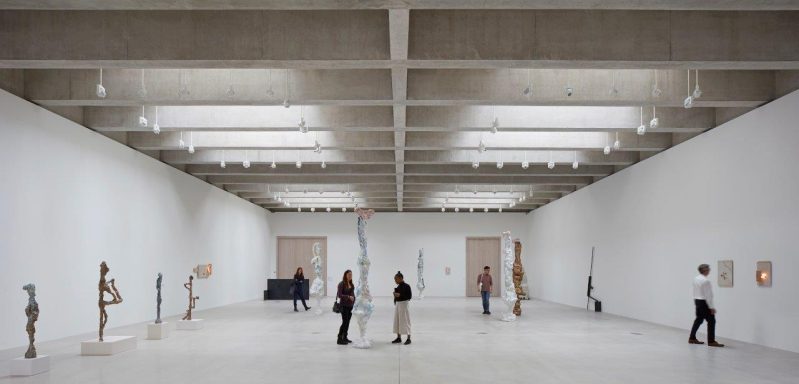 Art gallery interior with several sculptures and visitors engaging with the artwork.