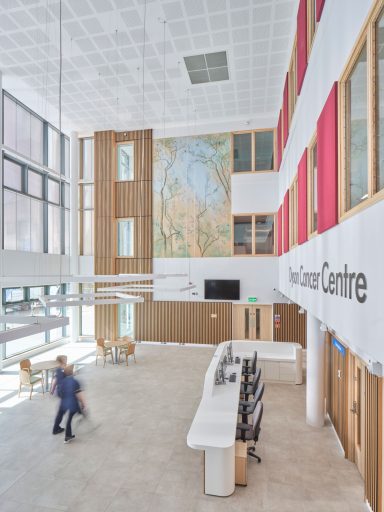 Modern atrium with a reception desk, large windows, and a mural on the wall.
