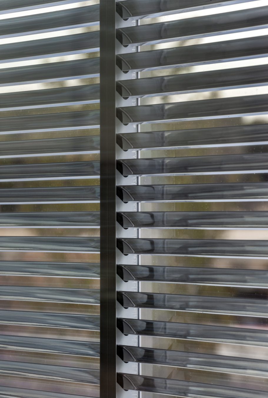 OKASOLAR W Close-up of horizontal blinds with a blurred outdoor view in the background.