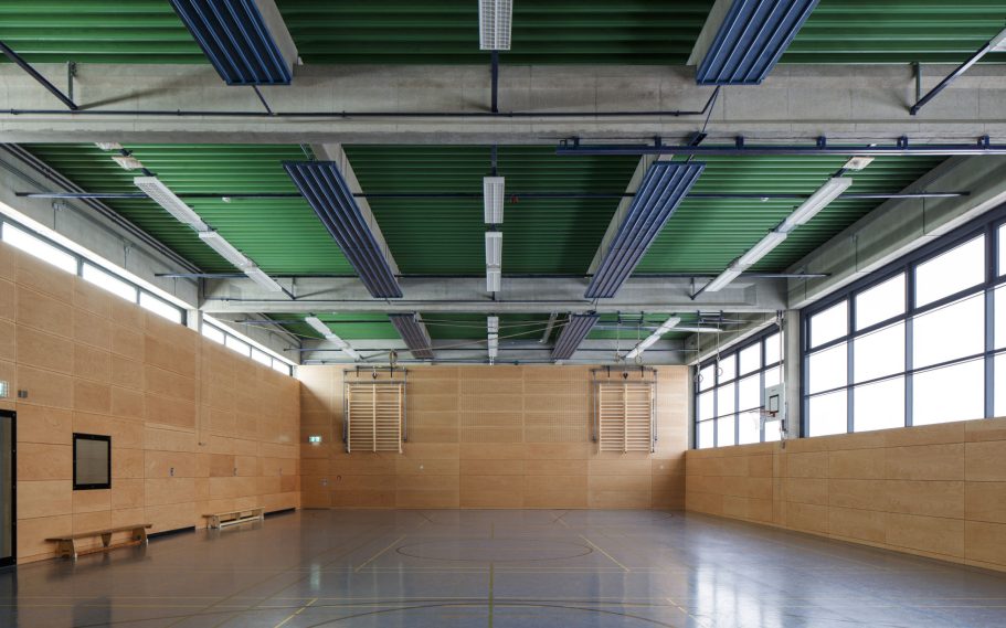 Sports Hall Lise-Meitner School, Köln, Germany Spacious interior with wooden walls and a high ceiling featuring green panels.