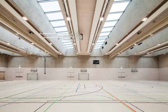 Spacious indoor sports hall with skylights and marked court lines on the floor.
