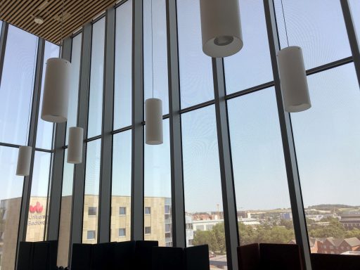 Modern interior with cylindrical white lights and large glass windows with a metal mesh interlayer offering a clear city view.