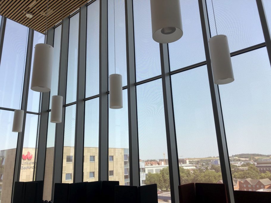 University of Bedfordshire Interior view with large glass windows and hanging cylindrical light fixtures.