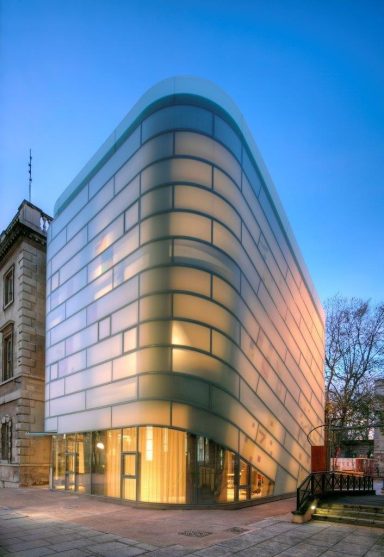 Modern glass building with curved facade, illuminated in soft evening light.