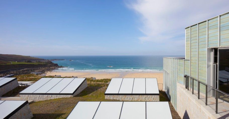 Tate St Ives, UK View of a beach with waves, surrounded by modern buildings and clear blue skies.