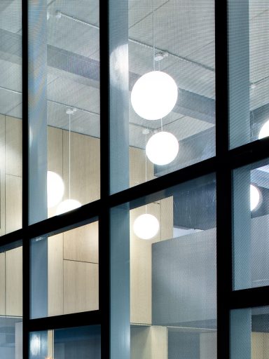 Interior of a building featuring large windows glazed with glass and expanded metal mesh and round ceiling lights.
