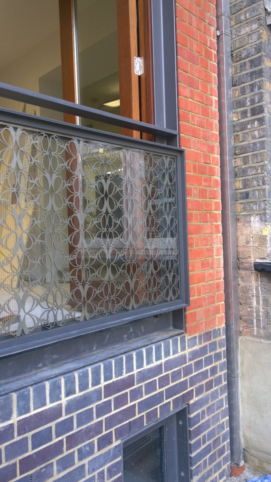 Welbeck Street, London Balcony railing with a patterned metal design, adjacent to brick and stone walls.
