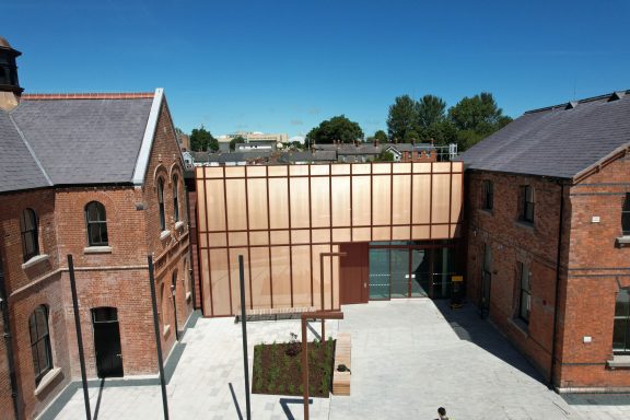Modern copper mesh-clad building adjacent to historic red-brick structures and a courtyard.