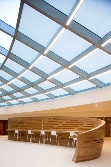 Modern interior with a wooden curved bar and skylight, creating a bright, spacious environment.