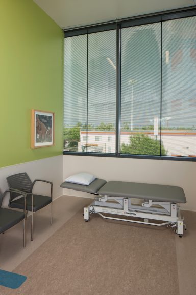 Seating area in a bright, modern room with large windows and a treatment table.